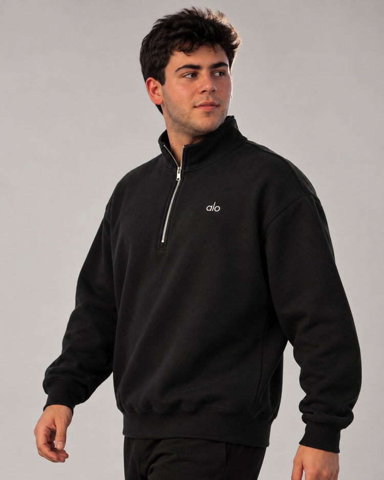 Modelo caminando con sudadera ALO Accolade 1/4 Zip negra, vista de tres cuartos